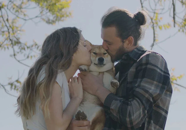 Two pet parents holding and kissing their dog outdoors