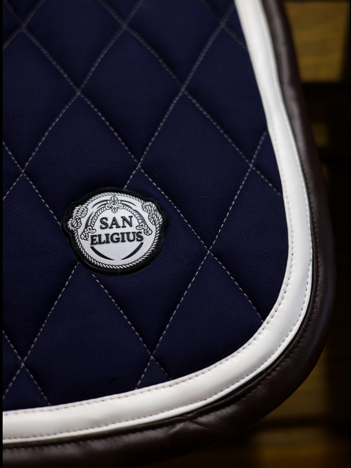 San Eligius navy quilted jump saddle pad with white and brown leather piping, detail of logo emblem